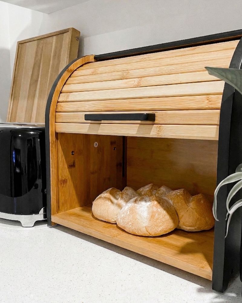 Black bread box open with loaves, beside a toaster