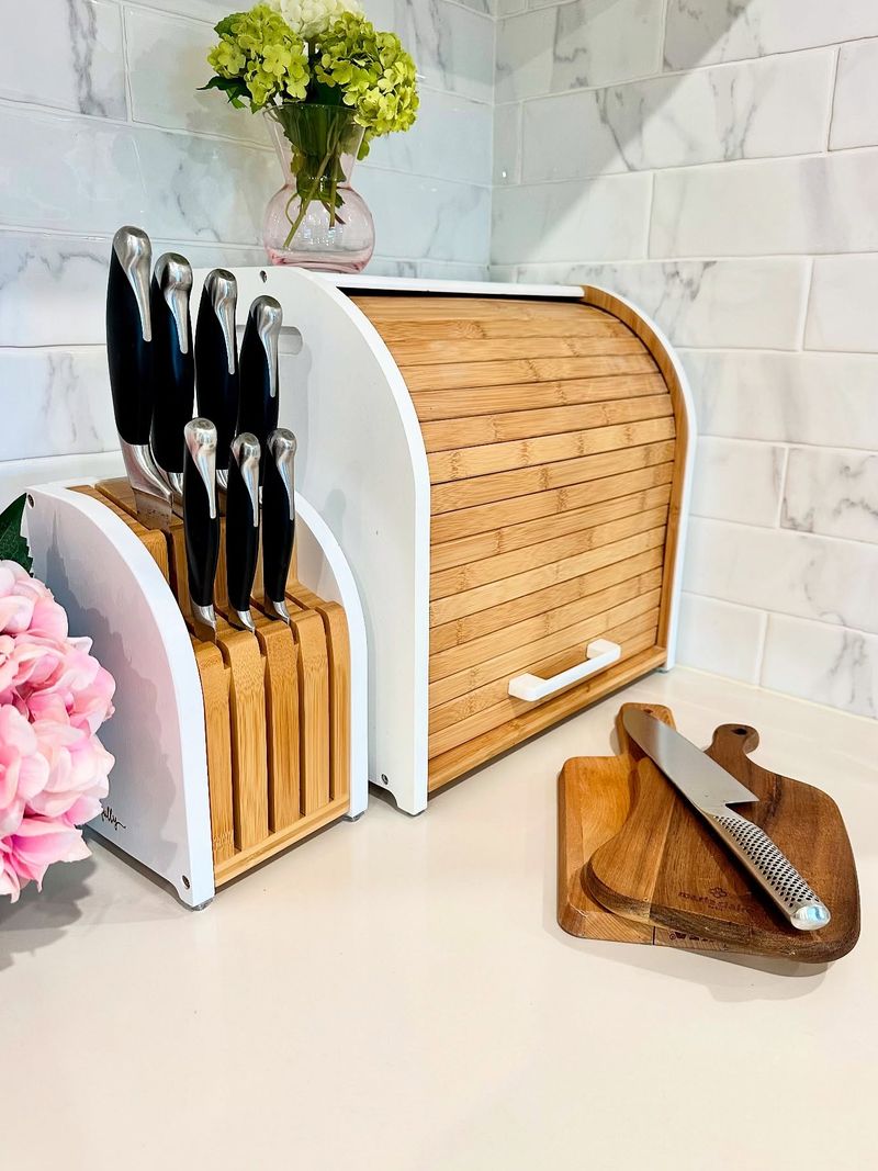 The knife block beside the White bread box on a marble bench with pink flowers